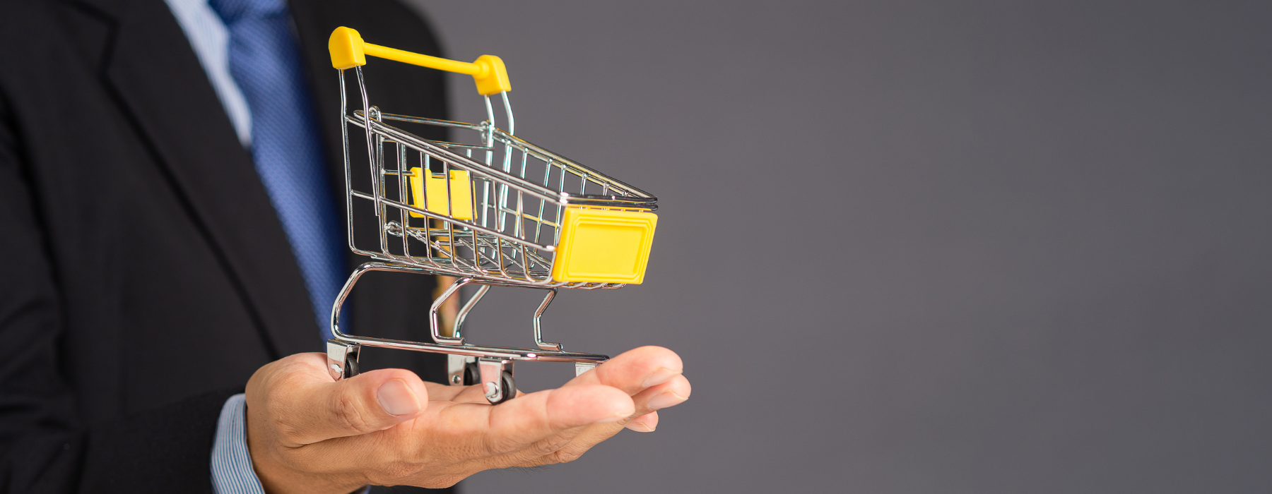 Homem de terno segurando um carrinho de compras em miniatura na palma da mão, representando estratégias e tecnologias do varejo. - agentic commerce