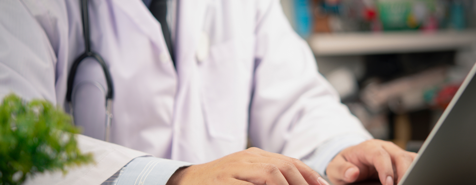 Profissional de saúde com jaleco e estetoscópio utilizando laptop em ambiente clínico.